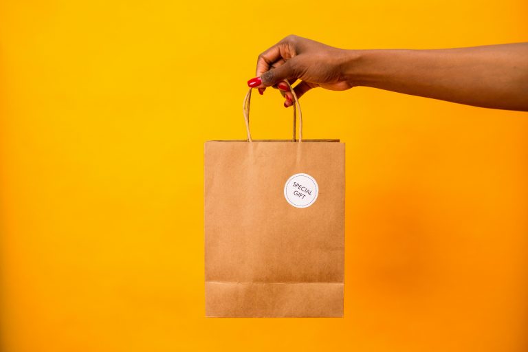 A woman's hand holding a brown paper gift bag labeled 'Special Gift' against a vibrant yellow backdrop.