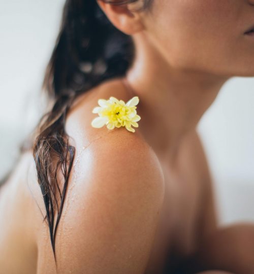 Close-up of a woman relaxing in a bath with a yellow flower on her shoulder.